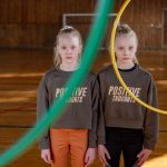 Twins stand indoors with hula hoops, promoting positive thoughts and teamwork.